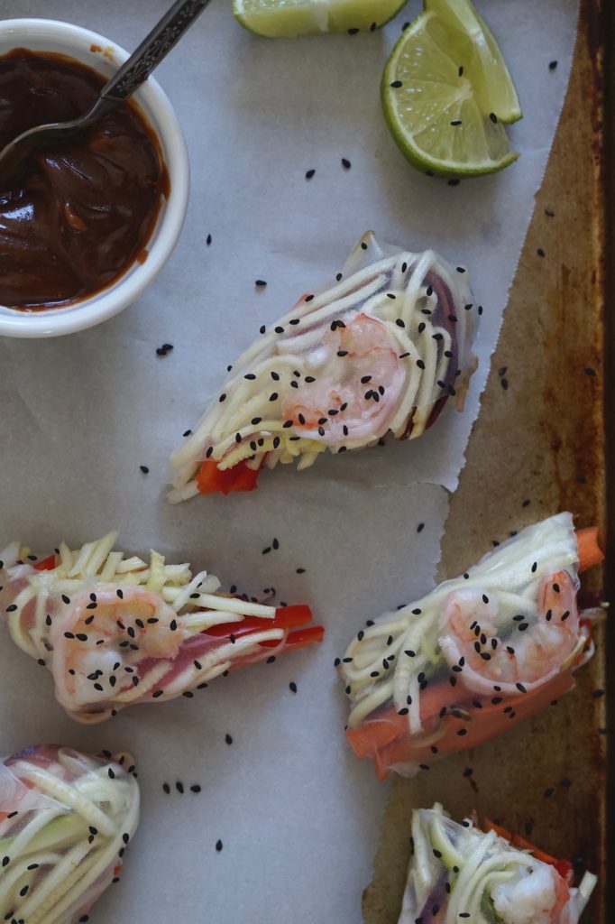 Fresh shrimp spring rolls on a tray with peanut sauce and sesame seeds.