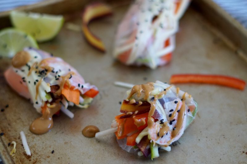 Fresh shrimp spring rolls on a tray with peanut sauce and sesame seeds.