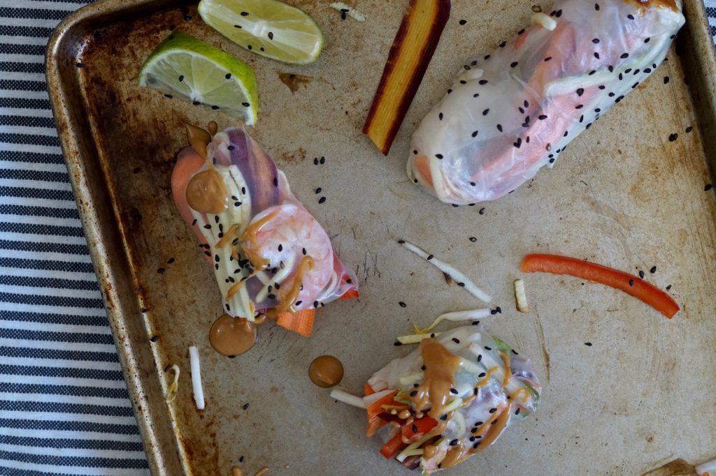 Fresh shrimp spring rolls on a tray with peanut sauce and sesame seeds.