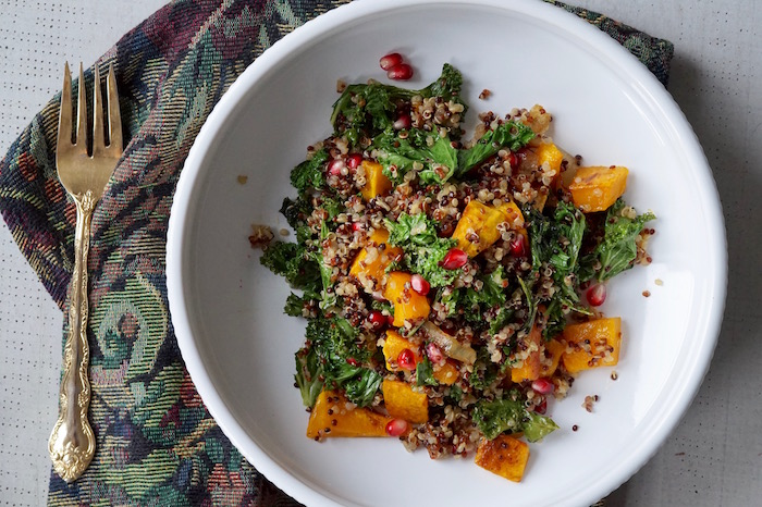 Kale salad with quinoa, butternut squash, pomegranate seeds, and onions in a bowl.