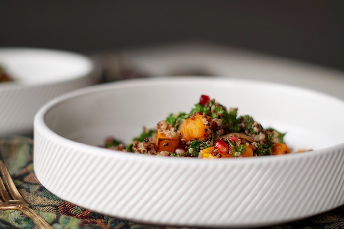 Kale salad with quinoa, butternut squash, pomegranate seeds, and onions in a bowl.