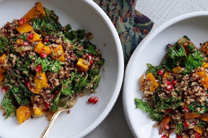 Kale salad with quinoa, butternut squash, pomegranate seeds, and onions in a bowl.