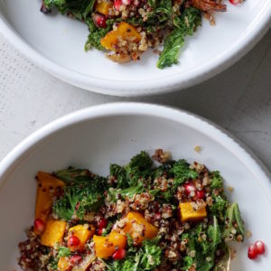 Kale salad with quinoa, butternut squash, pomegranate seeds, and onions in a bowl.