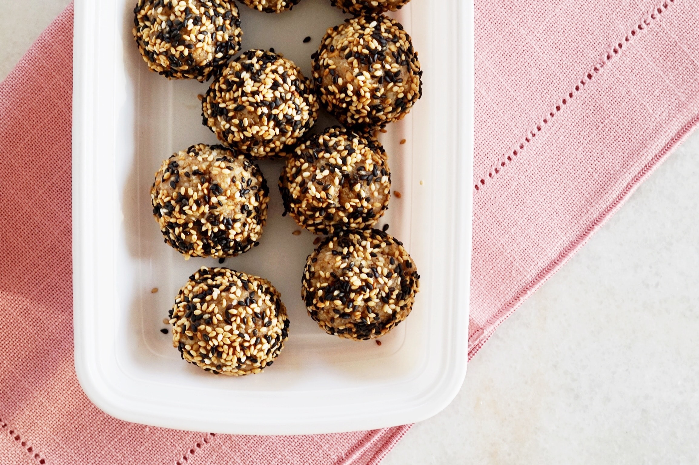 Sesame walnut balls inside a white container, over a pink napkin.