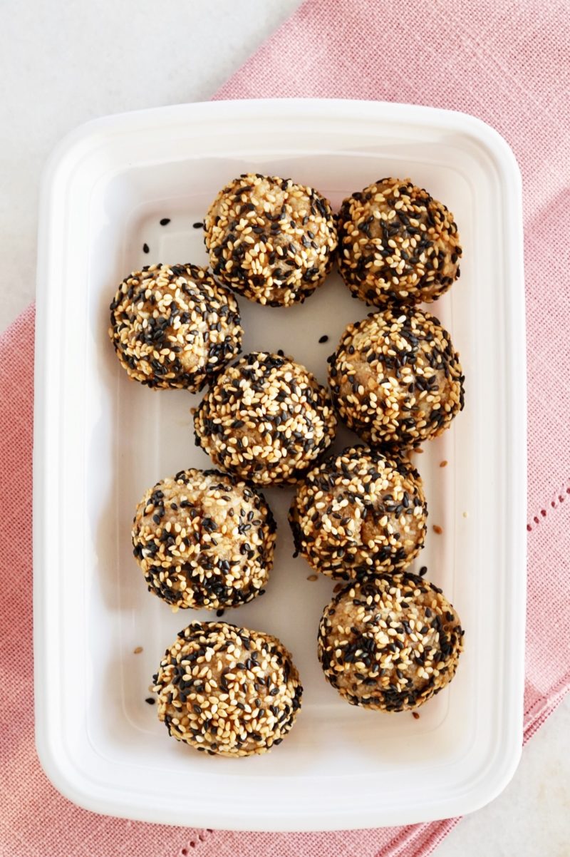 Sesame walnut balls inside a white container, over a pink napkin.