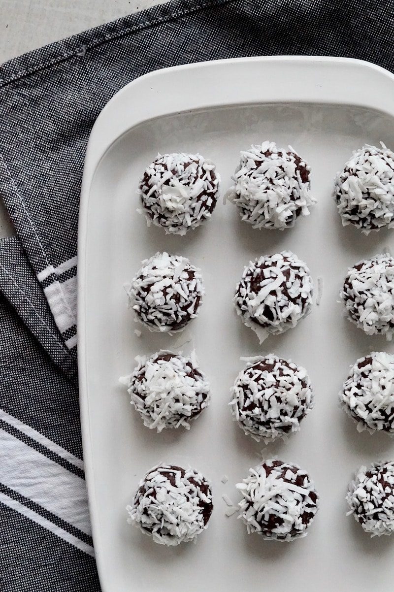 Salted chocolate brownie bites rolled in coconut shreds on a white plate.