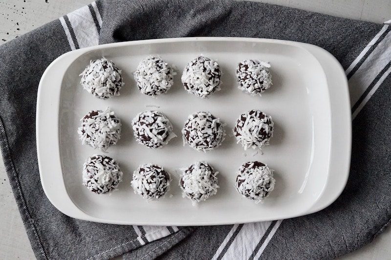 Salted chocolate brownie bites rolled in coconut shreds on a white plate.