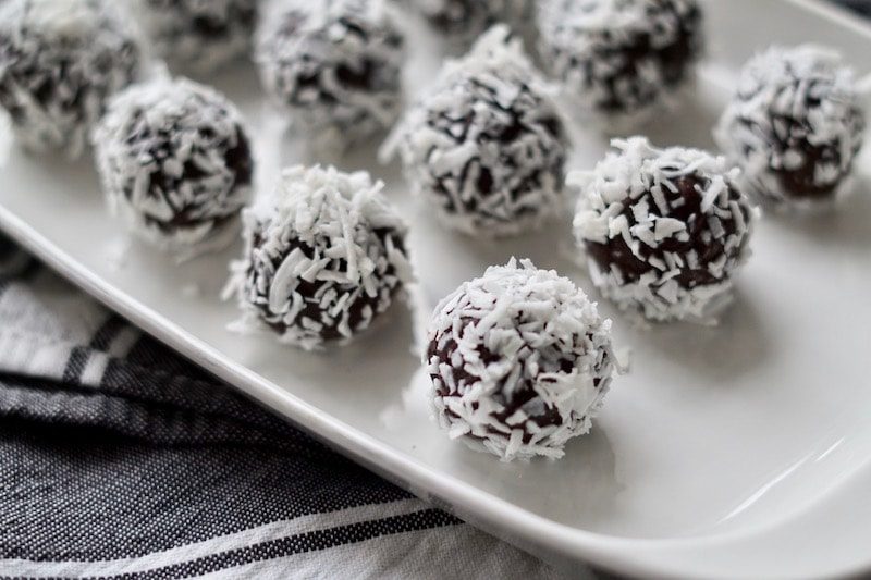 Salted chocolate brownie bites rolled in coconut shreds on a white plate.