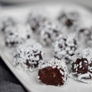 Salted chocolate brownie bites rolled in coconut shreds on a white plate.