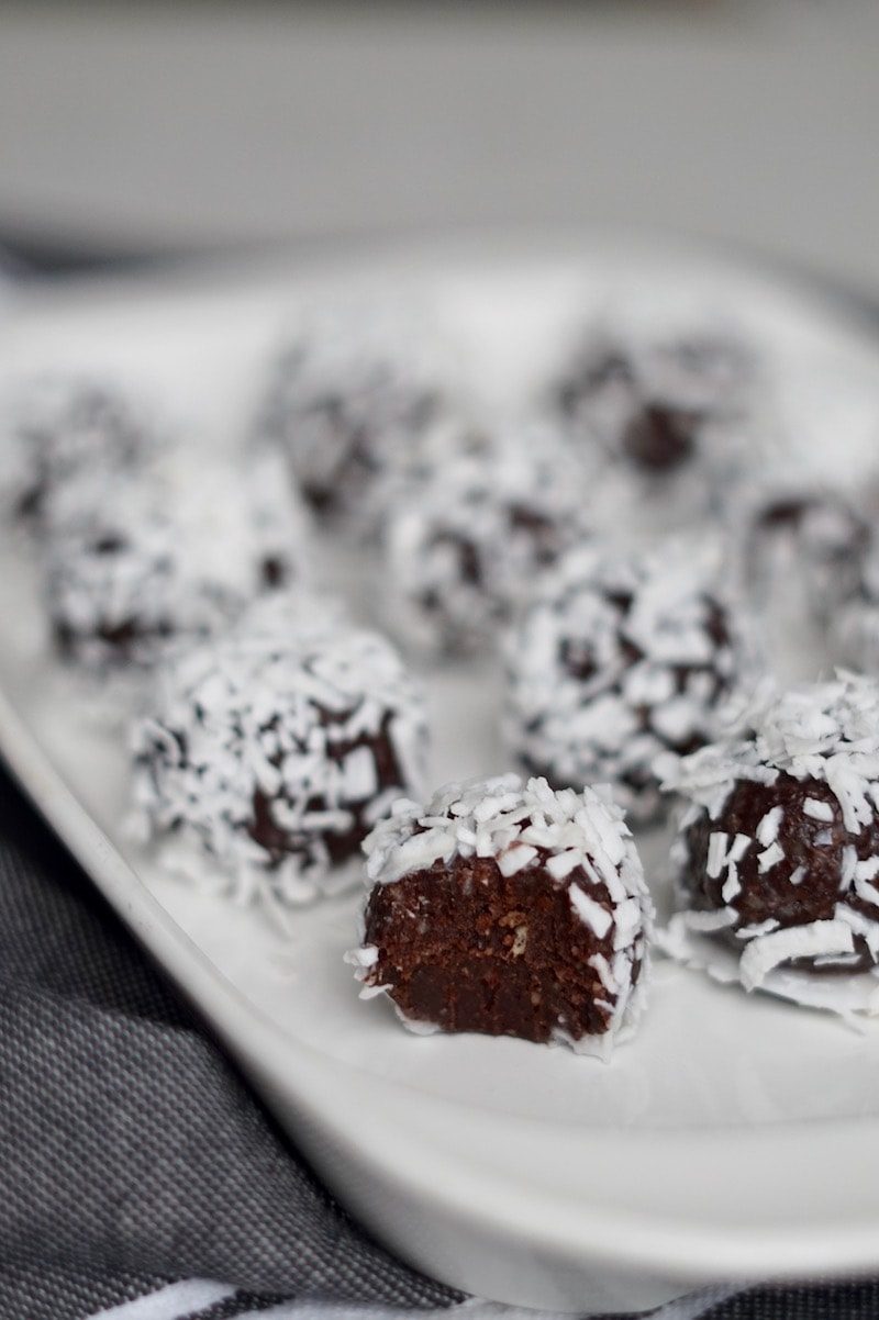 Salted chocolate brownie bites rolled in coconut shreds on a white plate.