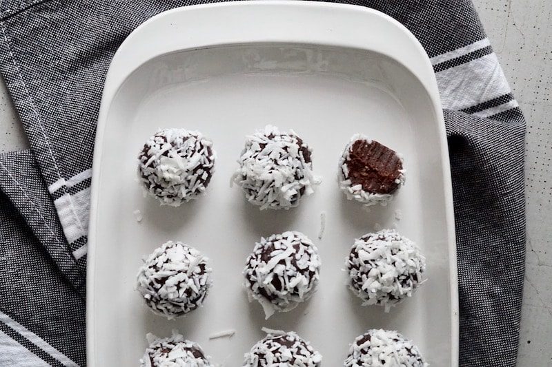 Salted chocolate brownie bites rolled in coconut shreds on a white plate.