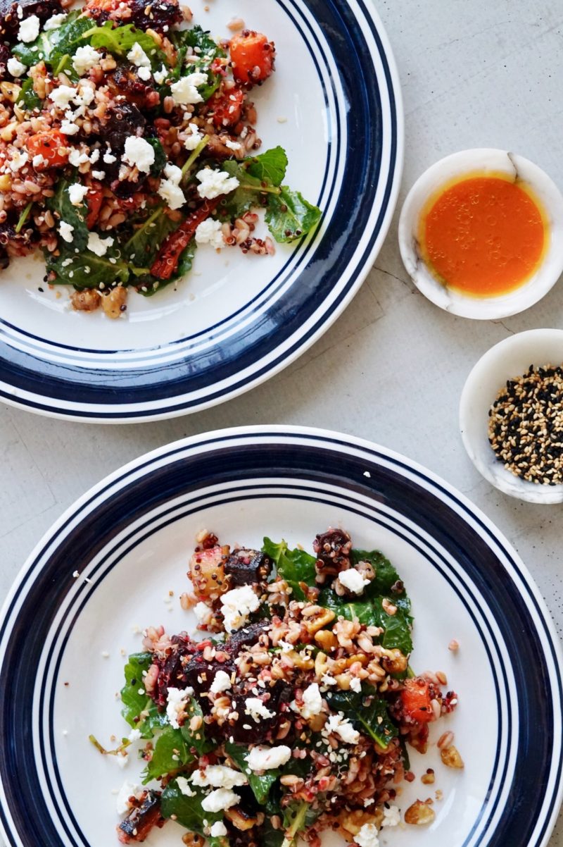 Salad with carrots, beets, blood oranges, grains, spinach, and ginger dressing on plates.