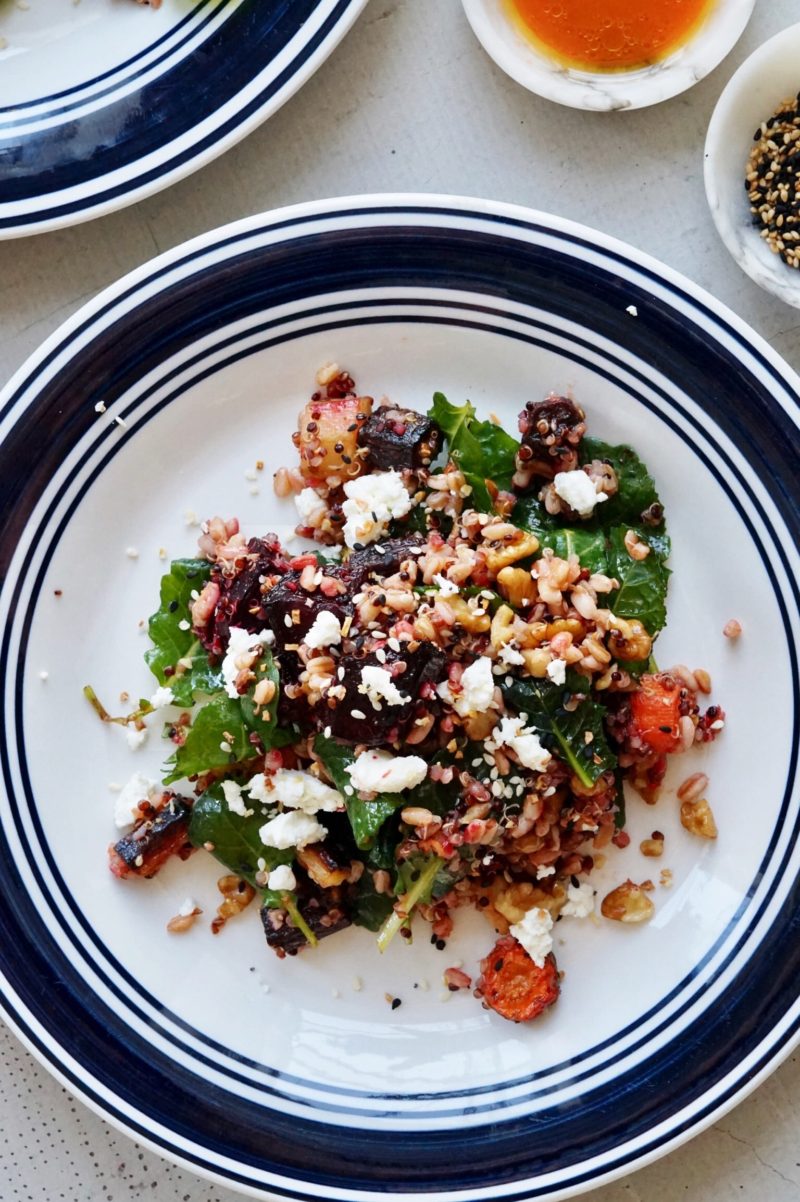 Salad with carrots, beets, blood oranges, grains, spinach, and ginger dressing on plates.