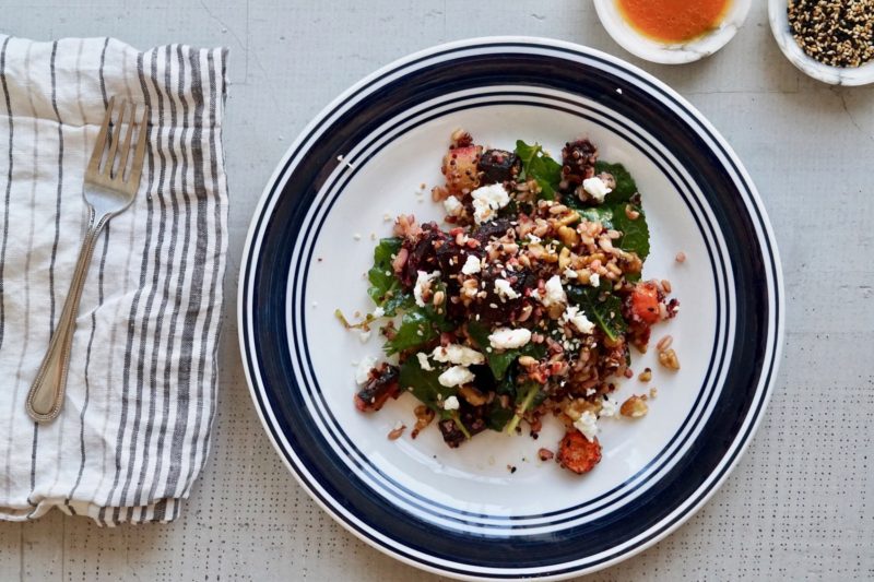 Salad with carrots, beets, blood oranges, grains, spinach, and ginger dressing on plates.