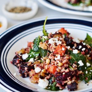 Salad with carrots, beets, blood oranges, grains, spinach, and ginger dressing on plates.