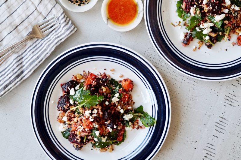 Salad with carrots, beets, blood oranges, grains, spinach, and ginger dressing on plates.